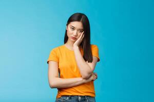 Sad bored asian female student attend boring uninteresting lecture lean face palm, look indifferent express apathy dislike, grimacing and sulking disappointed stand blue background bothered photo