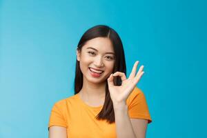 Close-up cute asian friendly girl supports your fantastic idea, smiling broadly, show okay ok sign approval, accept terms, agree take part event, stand blue background satisfied, judging nice work photo