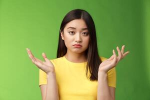 Close-up confused unemotive brunette woman spread hands sideways full dibelief, questioned what happening, look apathy reluctant, stand green background frustrated, no emotions photo