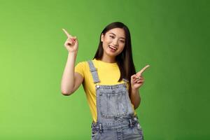 Friendly stylish good-looking upbeat teenage asian brunette, dancing joyfully showing few choices, shopping online easy picking products, pointing sideways left right, smiling enthusiastic photo