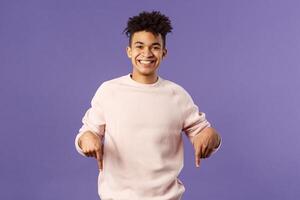 Portrait of cheerful, happy young 25s man recommending product, showing promo of product, delivery service, online shop or appllication, pointing fingers down, smiling pleased camera photo