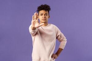 Portrait of confident serious-looking determined young man trying to prevent something, pull hand in stop gesture, look camera assertive, prohibit, give warning or forbid something photo