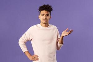 So what, why asking. Portrait of unbothered and careless, ignorant young man dont care on people rules, raising hand in dismay and confusion, being puzzled, look uninterested, purple background photo