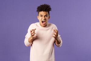 Portrait of hateful, outraged young hispanic man losing his temper, want to strangle or attack someone, cursing being aggressive, squeeze hands into fist from rage and hate, purple background photo