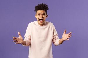 Portrait of concerned, upset and frustrated young man cant believe he lost, asking why, spread hands sideways in dismay, complaining shouting angry and uneasy, standing purple background photo