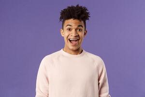 Close-up portrait of enthusiastic, excited and surprised hispanic guy hear amazing news, open mouth beaming smile from amazement and joy, rejoicing glad for friend achievement, purple background photo