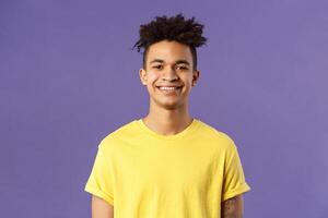 Close-up portrait of nice, friendly-looking hispanic male student in yellow t-shirt, grinning delighted, look upbeat happy and positive, standing enthusiastic with beaming smile purple background photo