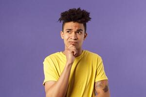 Close-up portrait of indecisive, puzzled attractive young man have problems, lacking idea, thinking, look away frowning and grimacing troubled, standing thoughtful purple background photo
