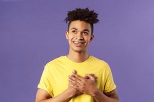 Close-up portrait of touched, romantic attractive man, hold hands on heart, remember nice lovely memory, looking up daydreaming, smiling pleased, appreciate something, purple background photo