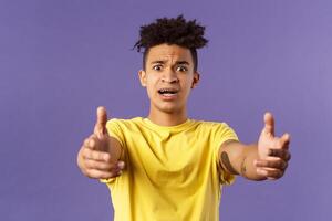 Waist-up portrait of concerned, nervous young man reaching hands forward to hold something but being scared, friend asking take baby for sec, standing very anxious and afraid, purple background photo