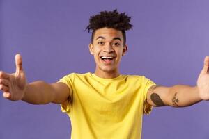 Close-up portrait of friendly cheerful young hispanic hipster guy giving warm welcome to dearest guests, spread hands sideways for greeting, cuddling or embracing person, smiling pleased photo