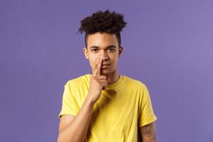 Close-up portrait of funny and unappropriate young hispanic teenage guy picking nose with finger, smiling and looking at camera, standing purple background, have bad habit photo