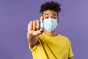 Medicine, coronavirus and people concept. Close-up portrait of young man in facial mask holding ampoule with drug, finally found vaccine from covid19, standing purple background photo