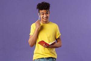 Young troubled male student studying, doing homework, scratch head indecisive and unsure, facing complicated task, dont know how solve equation, grimacing, holding notebook, thinking photo