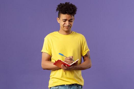 Portrait of unamused, displeased and bothered young man having troubles with homework, smirk and grimacing, trying solve math equation, writing down in notebook, fill-in schedule photo