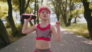 Sport runner jogger child girl listen bluetooth music speaker dancing to camera having fun in park video
