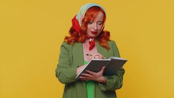 Thoughtful journalist redhead woman making notes, writing down thoughts with pen into notebook diary video