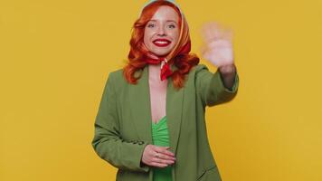 Redheaded woman smiling friendly at camera and waving hands gesturing hello or goodbye, welcoming video