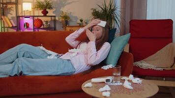 Sick ill child kid suffering from cold or allergy lying on home sofa sneezes wipes snot into napkin video