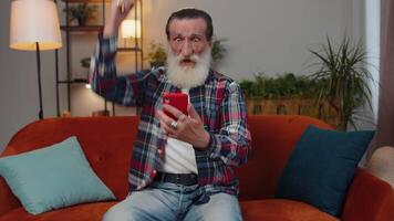Senior grandfather at home use smartphone typing browsing, wow yes found out great big win celebrate video