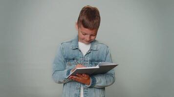 Thoughtful toddler kid boy making notes writing down thoughts in notepad notebook diary, to do list video