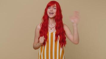 Redheaded woman smiling friendly at camera and waving hands gesturing hello or goodbye, welcoming video