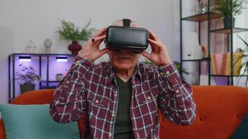 Senior man using VR headset helmet app to play simulation game watching virtual reality home video