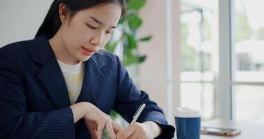 Portrait of Asian businesswoman in suit sits on table while analyze documents and taking notes in small coffee shop. Work from anywhere, Remote working photo