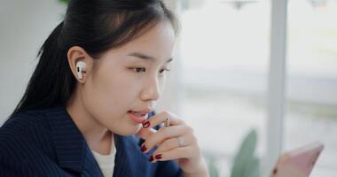 Selective focus, Asian businesswoman in suit wear wireless headphones talk about work via mobile phone in small coffee shop. Work from anywhere, Remote working photo