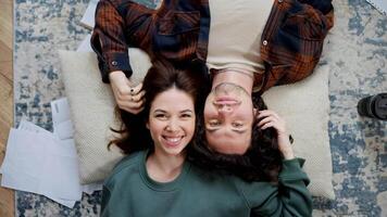 Top view rotating camera happy brunette girl holding and touching hair of her boyfriend with curly hair lying on pillow head to head on floor in modern apartment at home video