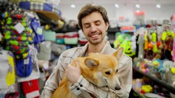 Portrait of a happy brunette guy in a plaid shirt who holds his yellow corgi dog in his arms in a pet store video
