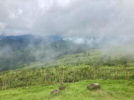 The mist flows through the mountain forest, Sun shining into tropical forest, Mist drifts through mountain ridges in the morning, slow floating fog blowing cover on the top of mountain photo