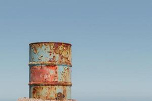 A weathered oil drum stands tall, showcasing vibrant colors and a distinct logo under a bright blue sky, evoking a sense of isolation and resilience in nature. photo