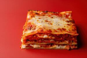 A delicious slice of lasagna showcases layers of rich meat, cheese, and sauce against a striking red backdrop. photo