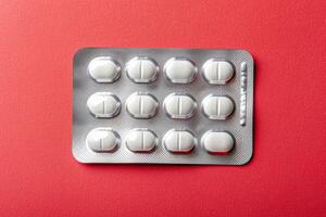 A blister pack containing twelve white pills is displayed on a bright red backdrop, highlighting the contrast and simplicity of the design. photo