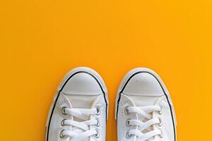 A pair of pristine white sneakers lies isolated on a vibrant yellow backdrop, showcasing their modern design and versatility. photo