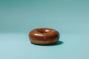 An isolated chocolate-covered donut rests elegantly against a soothing turquoise backdrop, inviting indulgence. photo