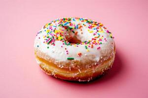 A delightful glazed donut topped with vibrant sprinkles rests against a soft pink backdrop, ready to be enjoyed. photo
