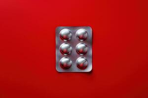 A blister pack containing six shiny white pills rests against a vibrant red backdrop, creating a striking contrast that draws attention. photo