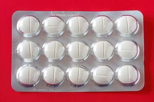 An isolated blister pack containing white pills is prominently displayed against a striking red surface, creating a compelling visual contrast. photo