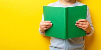 A pair of hands holding a open green book set against a yellow background photo