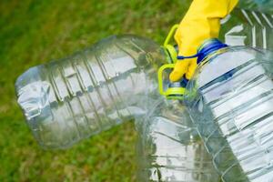 Garbage collection. Hand in yellow glove holding big empty plastic bottles. Grass on a background. photo