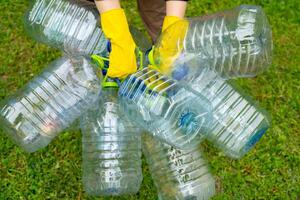 Garbage collection. Hands in yellow gloves holding big empty plastic bottles. Grass on a background. photo