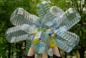 Garbage collection. Hands in yellow gloves holding big empty plastic bottles. Grass on a background. photo