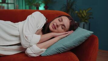 Tired young woman lying down in bed taking a rest at home, napping, falling asleep on orange couch video