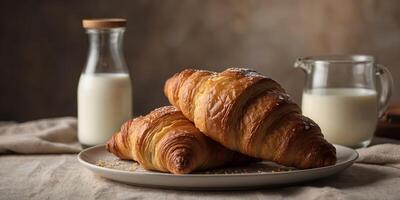 Two golden brown croissants are presented on a plate, accompanied by a bottle and a glass of milk, creating a simple yet appetizing breakfast scene. photo