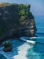 Touristic place and balinese temple. Scenic cliff with morning light and ocean with waves in Uluwatu, Bali. photo