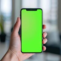 mobile phone with green screen. The gadget is held by hand on a blurred office background. Phone mockup. photo