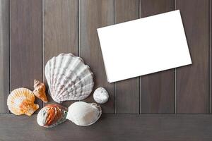 Top view of different sea shells with empty white note paper on wooden background. Summer time concept photo