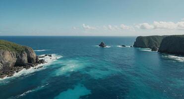 A serene ocean view from a high vantage point, showcasing calm, turquoise waters extending to the horizon under a light blue sky Rocky outcrops are visible near the bottom of the image. photo